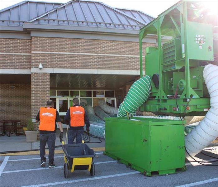 two technicians going into a commercial business in SERVPRO orange vests next to large green machine